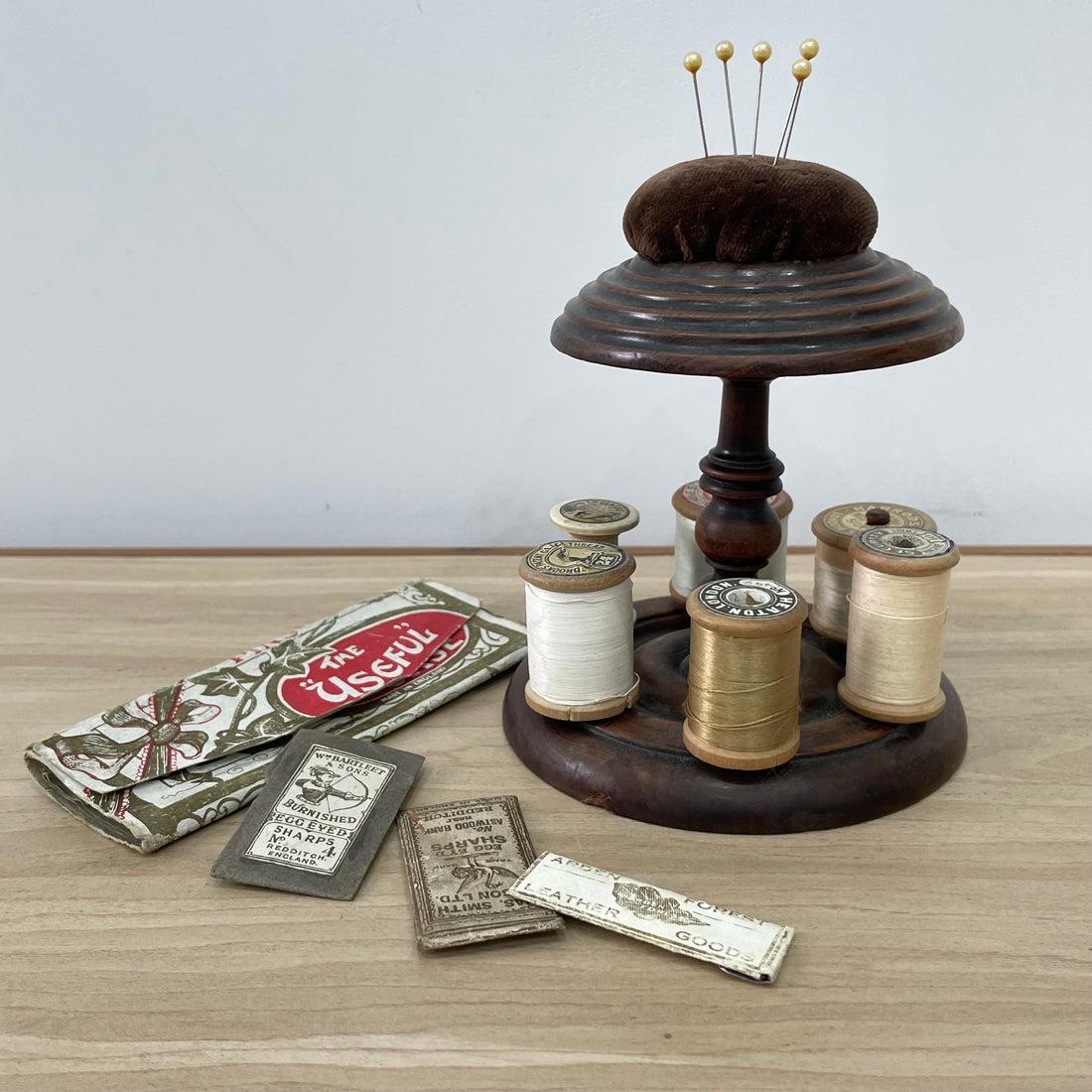 Vintage wooden sewing stand for six spools of thread and topped with a pin cushion.